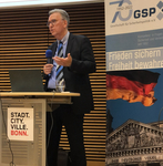 Ein Mann spricht an einem Pult mit Mikrofon, Laptop und einem 'STADT. BONN.' Schild. Ein GSP-Banner ist hinter ihm.