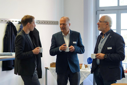 Drei Männer unterhalten sich bei einem Event mit Kaffeebechern in der Hand.