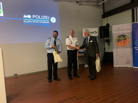 Zwei Polizisten und ein Mann im Anzug schütteln Hände, mit Polizeilogo und Bundeswehrverband-Banner im Hintergrund.