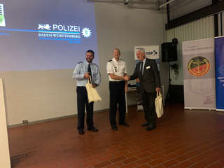 Zwei Polizisten und ein Mann im Anzug schütteln Hände, mit Polizeilogo und Bundeswehrverband-Banner im Hintergrund.