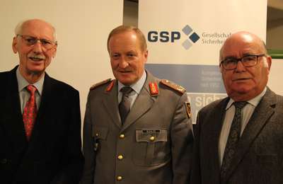 Drei Männer, darunter einer in Militäruniform mit Namensschild 'BÜHLER', stehen vor einem GSP-Banner.