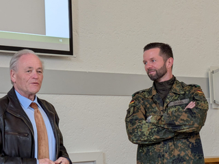 Ein älterer Mann in Zivil und ein jüngerer Mann in deutscher Militäruniform (Daniel) stehen nebeneinander, blicken nach links.