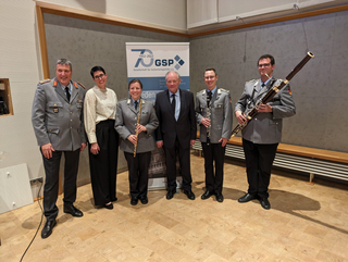 Gruppenfoto von sechs Personen, darunter Bundeswehr-Musiker mit Instrumenten und Zivilisten, vor einem GSP-Banner.
