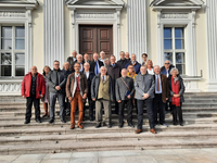 Gruppenfoto von Erwachsenen auf den Stufen vor einem prächtigen Gebäude im klassischen Stil mit Säulen.
