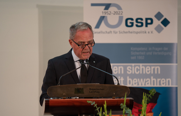 Ein Mann in Anzug und Brille spricht an einem Rednerpult des 'Bayerischer Landtag' vor einem GSP 70-Jahre-Banner.