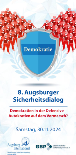 Schild 'Demokratie' von Angreifern umringt. 8. Augsburger Sicherheitsdialog: Demokratien defensiv. 30.11.2024.