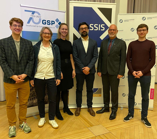 Sieben lächelnde Personen vor Veranstaltungsbannern, darunter GSP und Friedrich Naumann Stiftung.