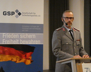 Ein Mann in Bundeswehruniform spricht an einem Rednerpult vor einem Banner der Gesellschaft für Sicherheitspolitik.