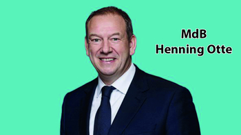 MdB Henning Otte, lächelt im Anzug vor türkisfarbenem Hintergrund.