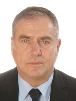 Porträt eines Mannes mittleren Alters mit kurzen grauen Haaren, hellen Augen, dunklem Anzug, blauem Hemd, dunkler Krawatte.