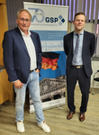 Zwei Männer lächeln vor einem GSP-Banner, das das 70-jährige Bestehen der Gesellschaft für Sicherheitspolitik feiert.