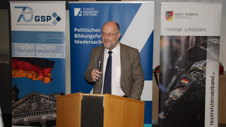 Mann hält Vortrag vor Bannern der GSP, Konrad-Adenauer-Stiftung und des Reservistenverbandes zu Sicherheitspolitik.