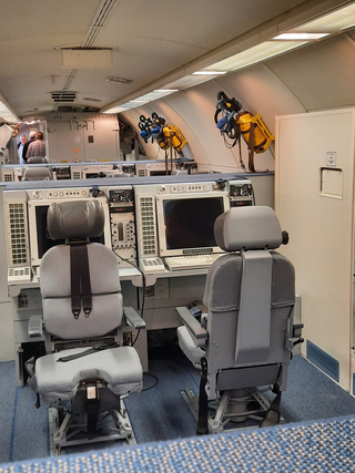 Innenansicht eines Spezialflugzeugs oder Kommandozentrale mit Bedienerstühlen, Bedienfeldern, Bildschirmen und Ausrüstung.
