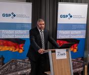 Ein Mann im Anzug spricht an einem Rednerpult vor GSP-Bannern, die die deutsche Flagge und den Reichstag zeigen.