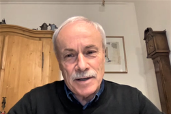 Ein älterer Mann mit weißem Haar und Schnurrbart in einem dunklen Pullover, blickt in die Kamera bei einem Videoanruf.