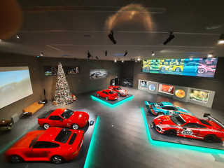 Blick von oben auf ein Porsche Museum mit Sportwagen auf beleuchteten Podesten, einem Weihnachtsbaum und großen Bildschirmen.