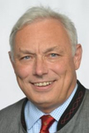 Porträt von Adolf Schöls, einem lächelnden älteren Mann mit weißen Haaren und traditioneller Jacke.