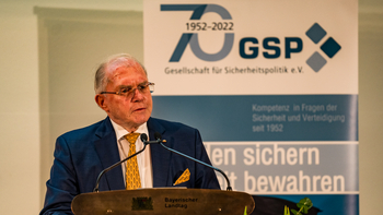 Älterer Mann im Anzug spricht am Pult des Bayerischen Landtags, im Hintergrund ein Banner der GSP (Gesellschaft für Sicherheitspolitik).
