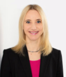 Lächelnde Frau mit langen blonden Haaren, trägt einen schwarzen Blazer über einem pinken Oberteil, vor weißem Hintergrund.