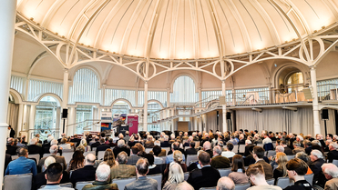 Zahlreiche Personen sitzen in einem großen, hellen Kuppelsaal und verfolgen eine Präsentation vor Bannern der Friedrich-Ebert-Stiftung.