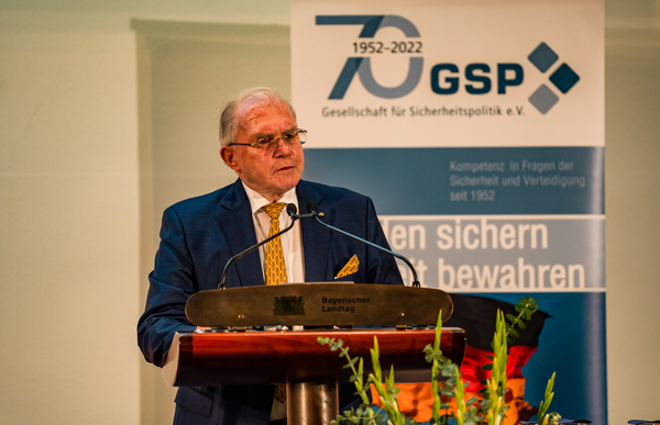 Älterer Mann im Anzug spricht an einem Rednerpult mit Mikrofonen, einem GSP 70-Jahre-Banner im Hintergrund.