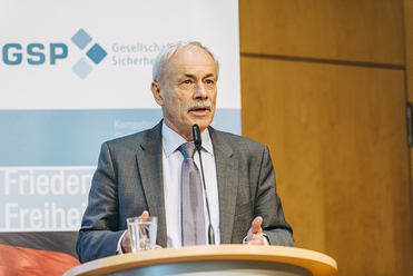 Ein Mann mit grauen Haaren und Schnurrbart spricht an einem Rednerpult mit Mikrofon vor einem GSP-Banner.