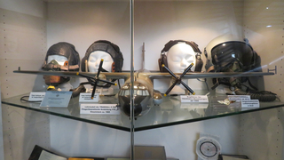 Modell einer Transall C-160 und verschiedene Fliegerhelme und Kopfhörer in einer Museumsvitrine.