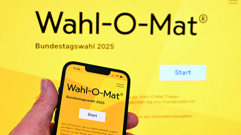 Hand hält Smartphone mit 'Wahl-O-Mat Bundestagswahl 2025' und 'Start'-Button, auf großem Bildschirm gespiegelt.