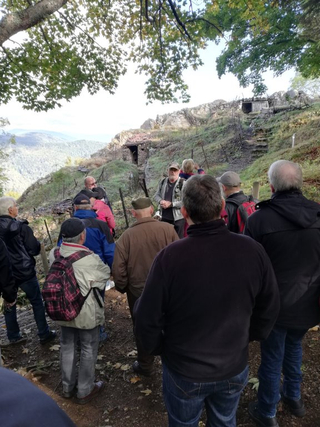 Gruppe auf einer Führung zu historischen Befestigungen auf einem felsigen, bewaldeten Hügel mit Bunkern, Blick ins Tal.