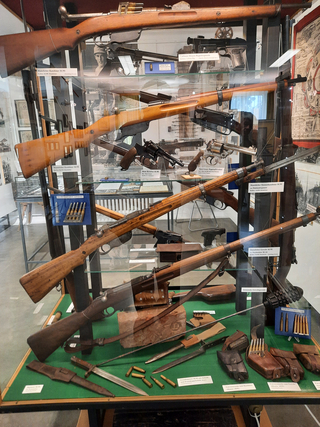 Ausstellung von historischen Schusswaffen und Militärausrüstung, darunter Gewehre, Pistolen, Revolver, Bajonette und Munition.