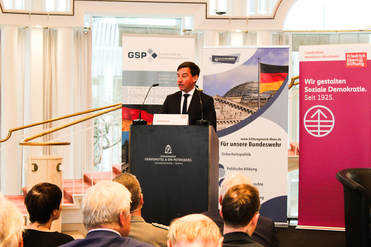 Mann spricht am Rednerpult vor Publikum. Im Hintergrund Veranstaltungsbanner von GSP, Bildungswerk und Friedrich-Ebert-Stiftung.