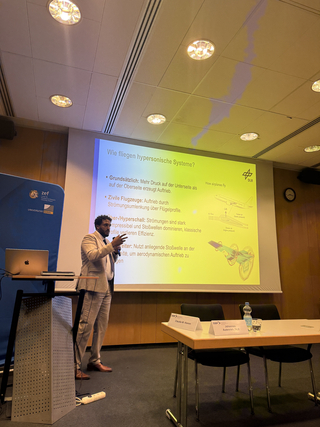 Ein Mann präsentiert über 'Wie fliegen hypersonische Systeme?' mit einer detaillierten Folie in einem Konferenzraum.