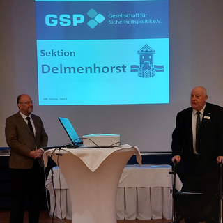 Zwei Männer stehen vor einer Leinwand mit dem Logo der GSP Sektion Delmenhorst bei einer Präsentation.