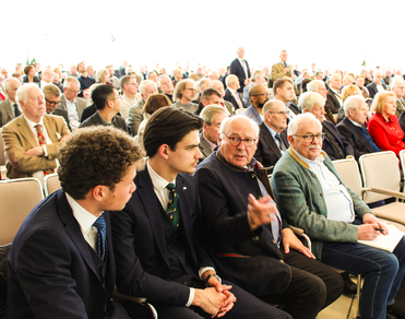 Eine große Gruppe von Menschen unterschiedlichen Alters, die in einem Auditorium sitzen und sich unterhalten.