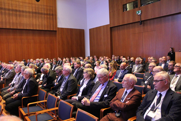 Personen bei einer Konferenz, sitzen in Reihen in einem Auditorium mit Holzwänden.