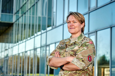 Eine lächelnde Frau in dänischer Tarnuniform mit verschränkten Armen steht vor einem modernen Glasgebäude.
