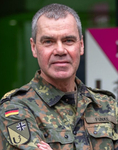 Porträt eines deutschen Militäroffiziers namens Funke in Flecktarn-Uniform, mit deutscher Flagge und Sanitätsdienst-Emblem.