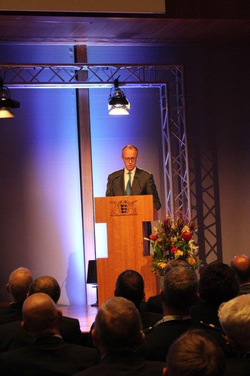 Friedrich Merz spricht an einem Holzpult mit Emblem vor Publikum bei einer formellen Veranstaltung.