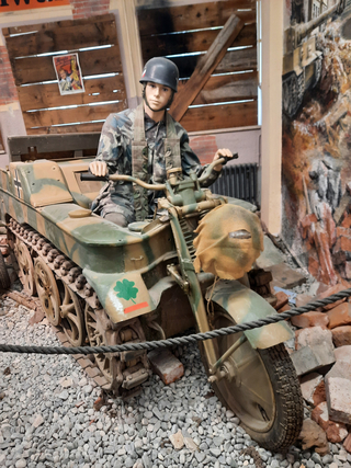 Deutsches Kettenkrad Halbkettenfahrzeug mit Soldaten-Schaufensterpuppe in Tarnuniform, in einer Museumskriegsszene.