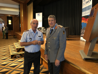 Zwei Männer in Uniformen stehen bei einer Veranstaltung vor einer Bühne mit Bannern der Friedrich Ebert Stiftung und GSP.