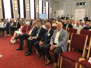 Publikum in einem Konferenzsaal: Zahlreiche Personen sitzen auf roten Stühlen bei einer Veranstaltung.