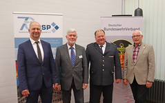 Vier Männer, darunter einer in Feuerwehruniform, stehen vor Bannern der Gesellschaft für Sicherheitspolitik und des Deutschen BundeswehrVerbandes.
