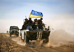 Ukrainische Soldaten auf einem gepanzerten Fahrzeug mit großer ukrainischer Flagge auf staubiger Straße im Militärkonvoi.