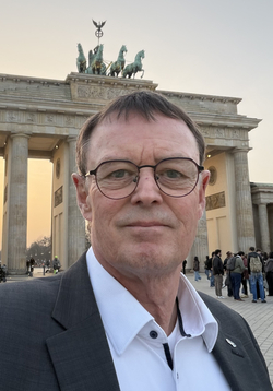 Selfie eines Mannes mit Brille vor dem Brandenburger Tor und der Quadriga bei Sonnenuntergang in Berlin.
