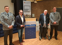 Vier Männer: zwei in Uniform, ein Redner mit Mikrofon, ein älterer Herr mit Rollator, bei einer Reservistenveranstaltung.