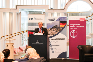 Mann Bartels spricht an Rednerpult, umgeben von Bannern des Bildungswerks, GSP und der Friedrich-Ebert-Stiftung.