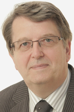 Porträtaufnahme eines Mannes mittleren Alters mit hellem Haar, Brille, Nadelstreifenanzug, gestreiftem Hemd und Krawatte.