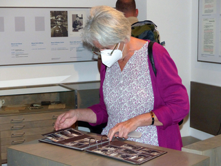 Eine Frau mit Maske blättert in einem Fotoalbum an einem Schalter in einer Ausstellung über historische Militärfiguren.