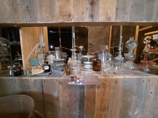 Antike Chemielaborausrüstung auf einem Holzregal, mit Kolben, Bechergläsern und Flaschen.