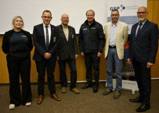 Sechs lächelnde Personen, darunter fünf Männer und eine Frau, stehen bei einer Veranstaltung der Gesellschaft für Sicherheitspolitik.